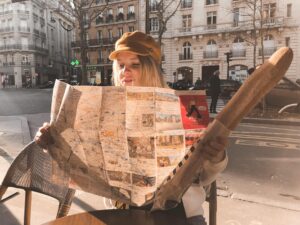 photo of sitting woman holding baguette while reading a map